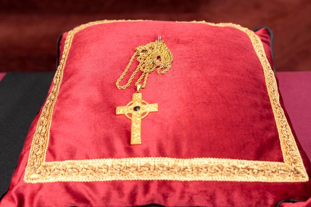 A gold pectoral cross on a red pillow